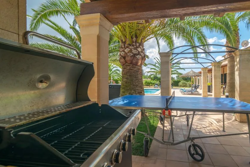 Una zona de cocina exterior cubierta da a una piscina y palmeras.