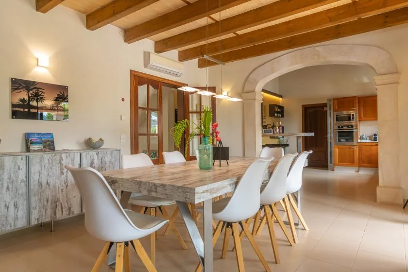 Un comedor con una mesa larga y asientos blancos bajo vigas de madera expuestas.