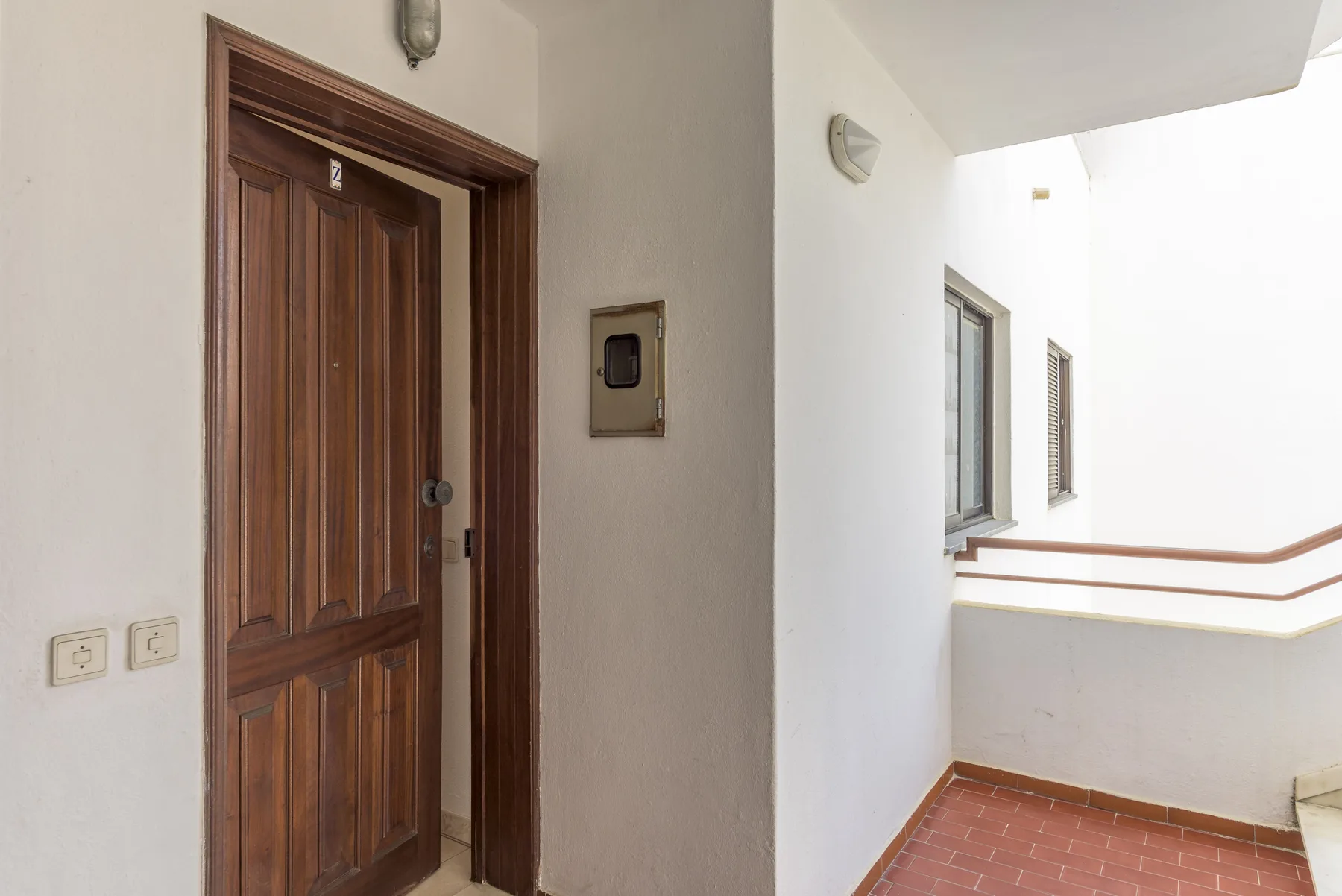 A tiled apartment corridor with a wooden door and white walls.