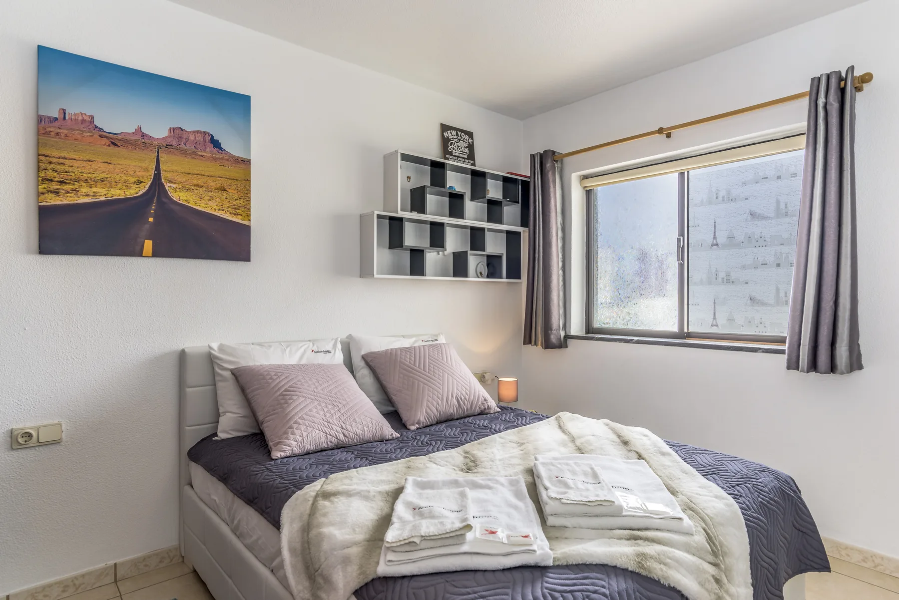 Un dormitorio con una cama bien hecha y una ventana grande.