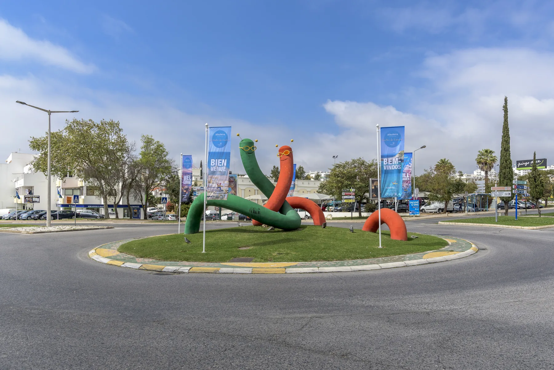 A roundabout with colorful inflatable sculptures and banners stands beneath a blue sky.