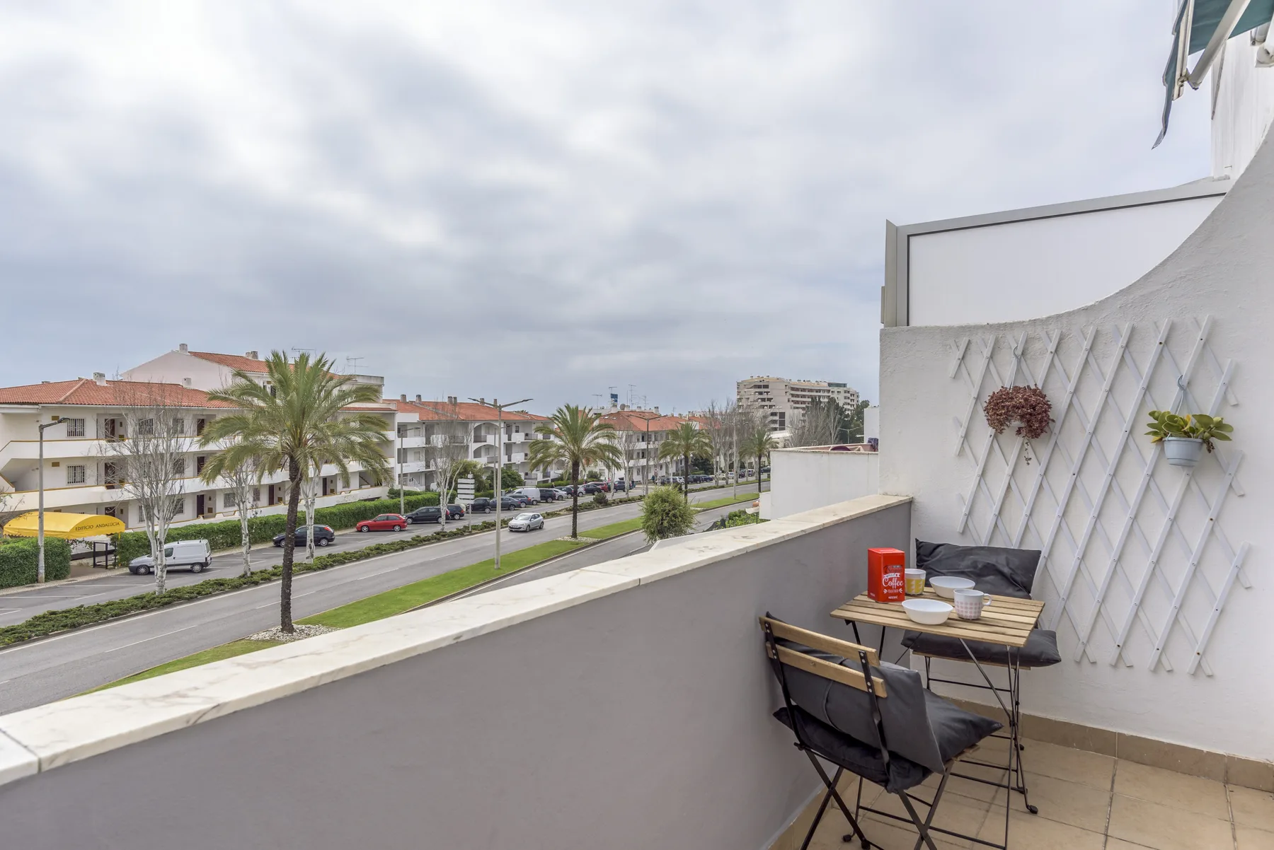 A balcony seating area overlooks a palm-lined road and nearby buildings.