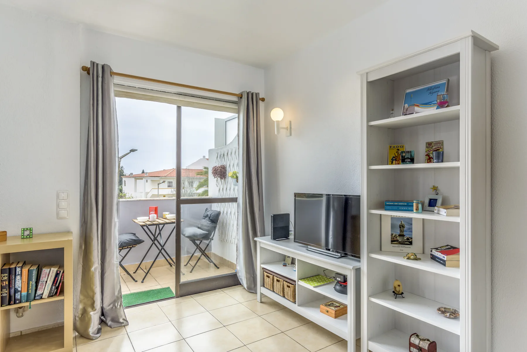 Living room with a television, shelving, and a glass door opening onto a balcony.