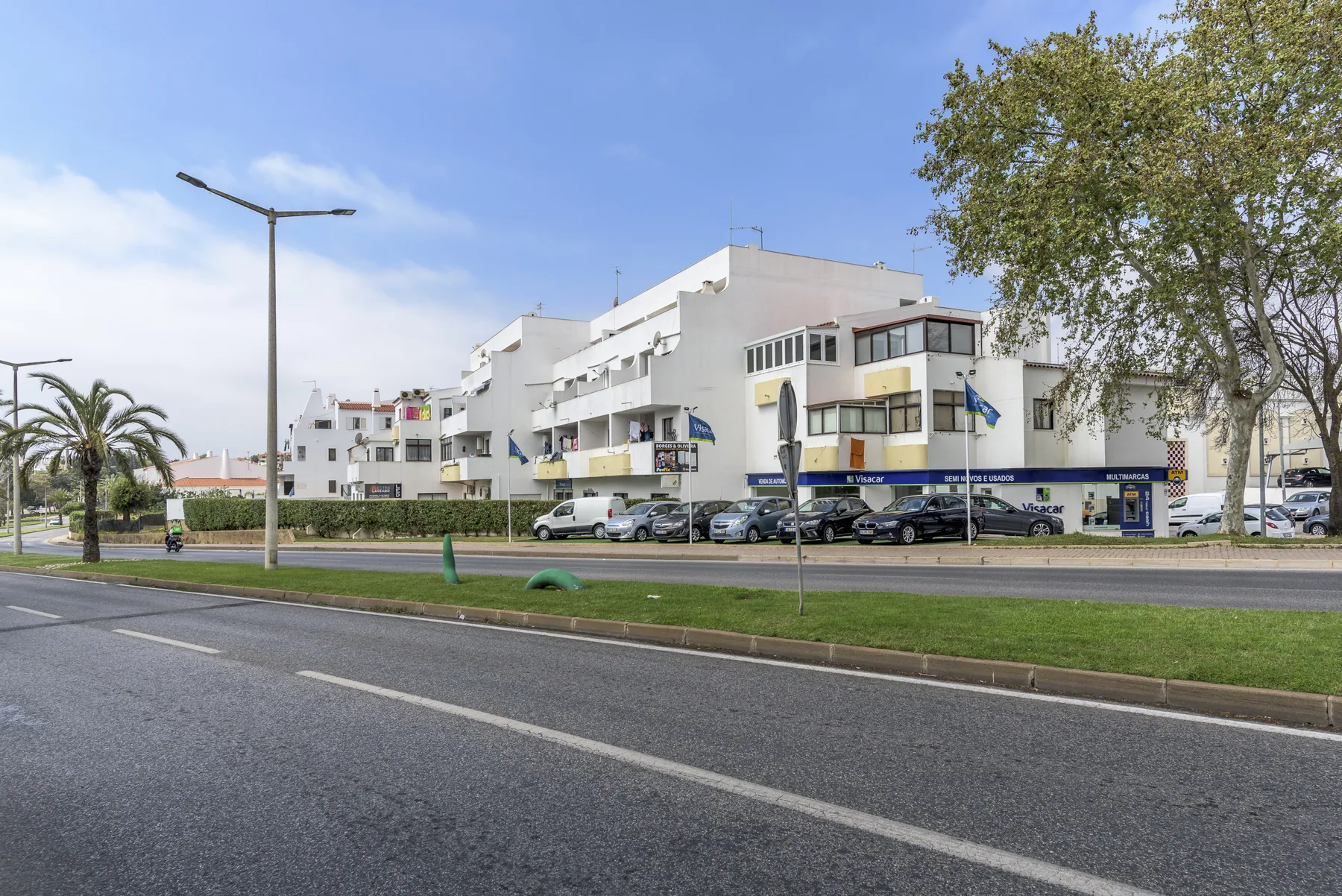 White apartment buildings stand beside a road and grassy verge.