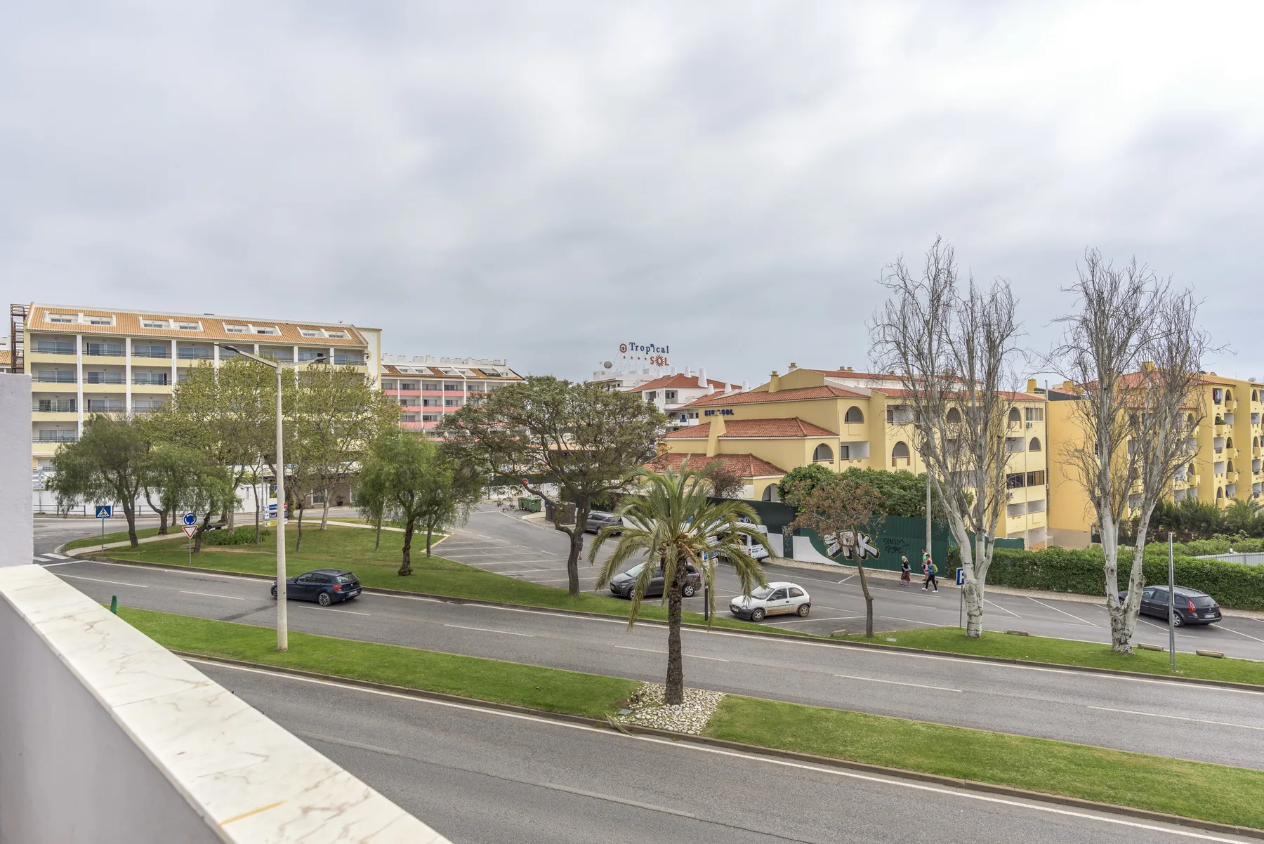 Un balcón da a una calle, árboles y edificios de apartamentos.