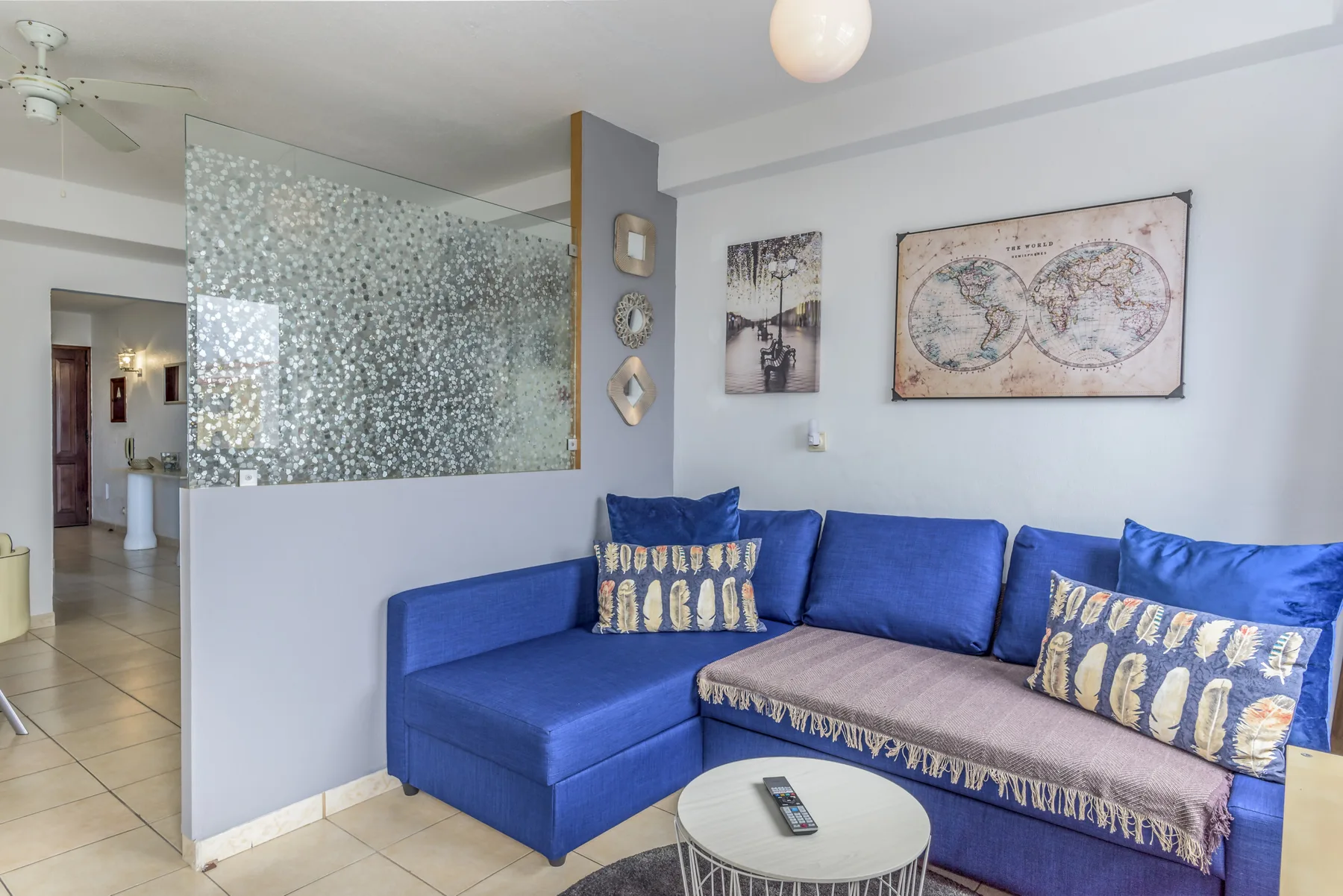 A living room with blue seating, patterned cushions, and framed wall art.