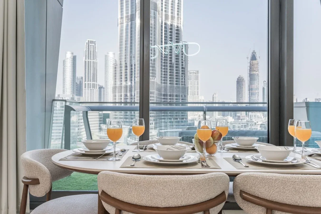 Una mesa está puesta junto a grandes ventanales con vistas al perfil urbano.