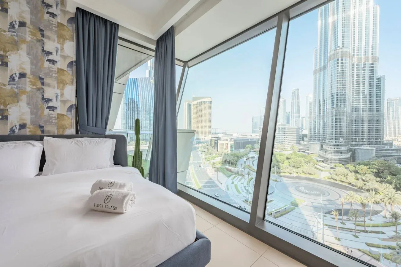 Un dormitorio con una cama bien arreglada junto a grandes ventanas con vistas a la ciudad.