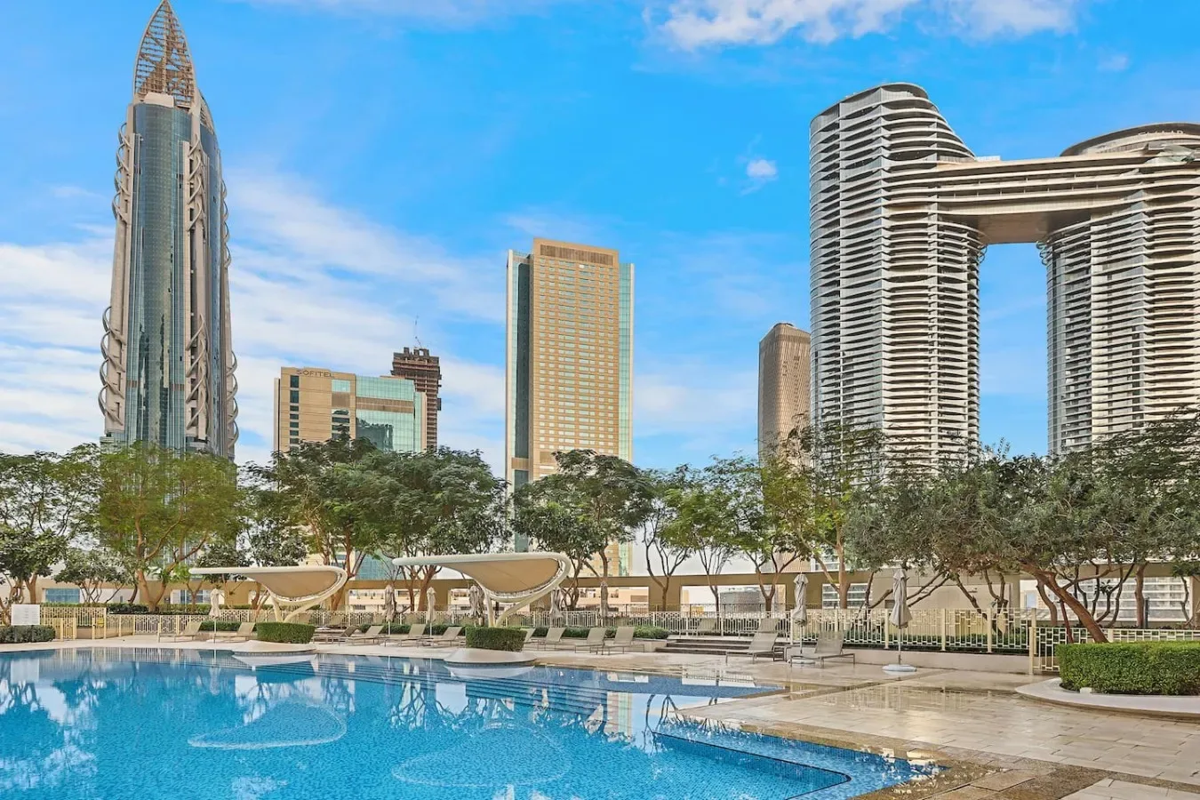 A swimming pool sits among landscaped grounds with high-rise buildings in the background.