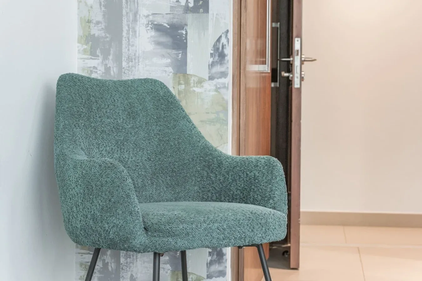 Una silla tapizada verde está junto a una puerta de madera abierta.