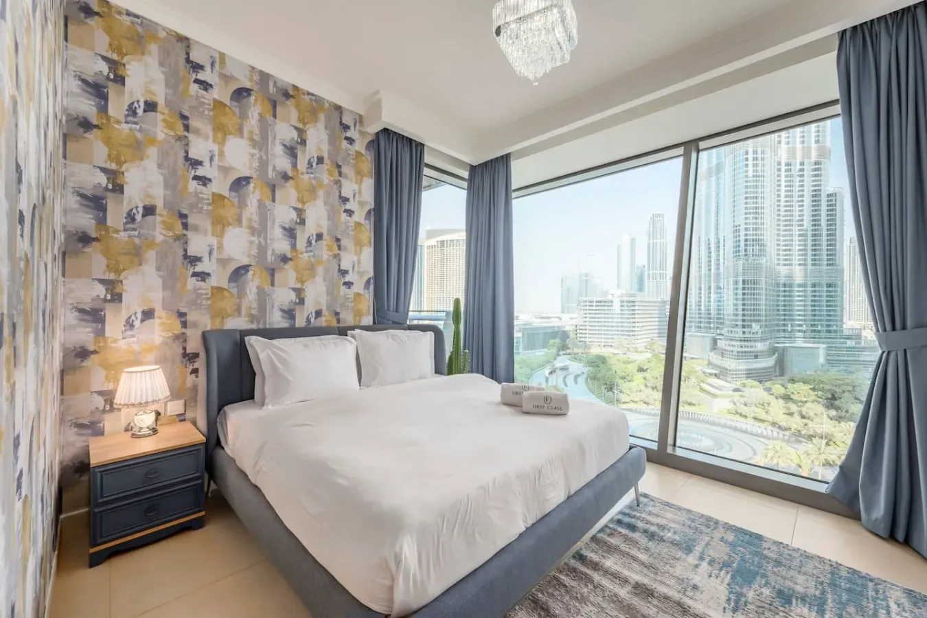 Un dormitorio con una cama tendida junto a grandes ventanas con vistas a edificios de la ciudad.