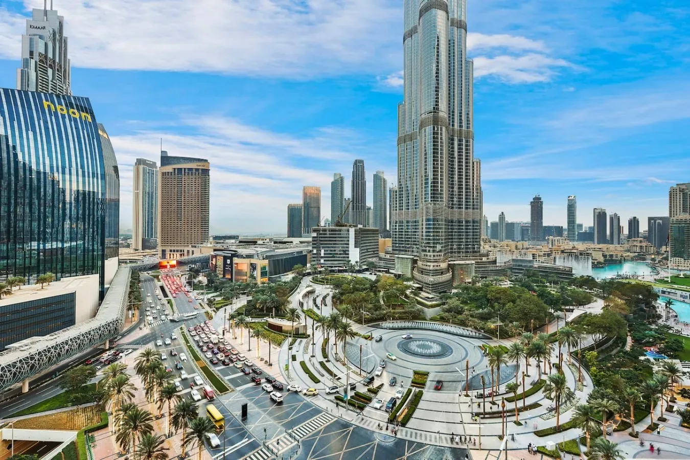 A city skyline surrounds a circular plaza with roads and palm trees.