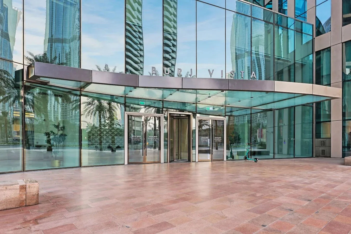 La entrada de un edificio moderno de vidrio da a una amplia plaza pavimentada.
