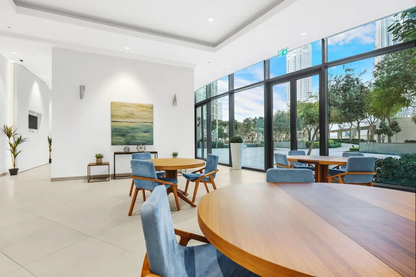 Un salón luminoso con mesas redondas y asientos junto a grandes ventanales.