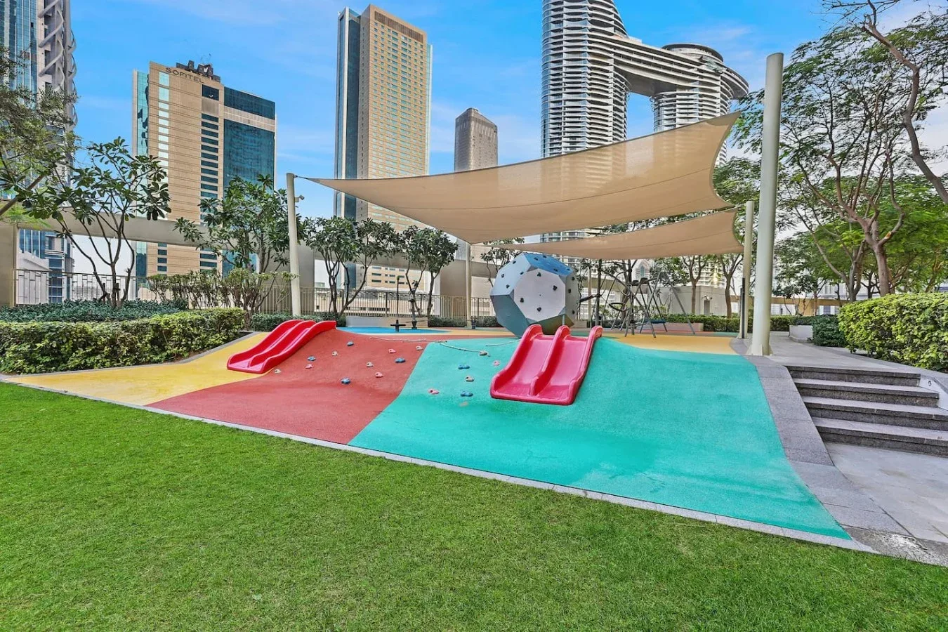 Un parque infantil al aire libre con toboganes de colores está bajo una cubierta de sombra.