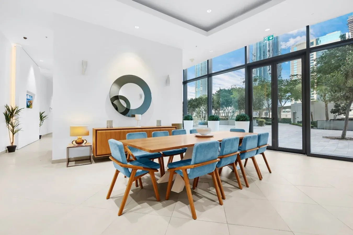 Un comedor luminoso con una mesa de madera, asientos azules y ventanales.
