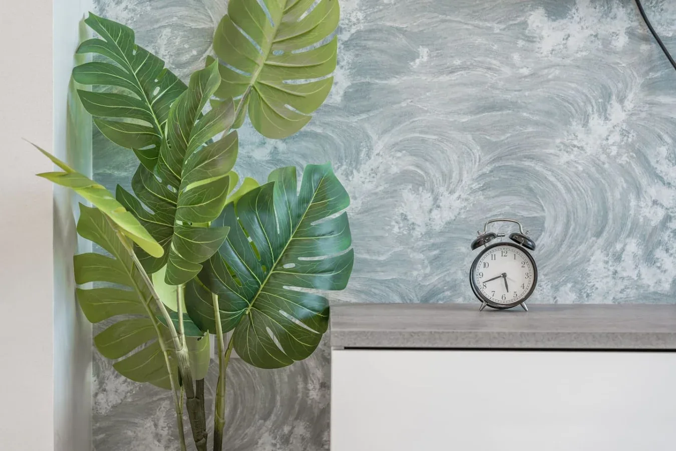 Una planta frondosa está junto a un pequeño reloj sobre una encimera de baño.