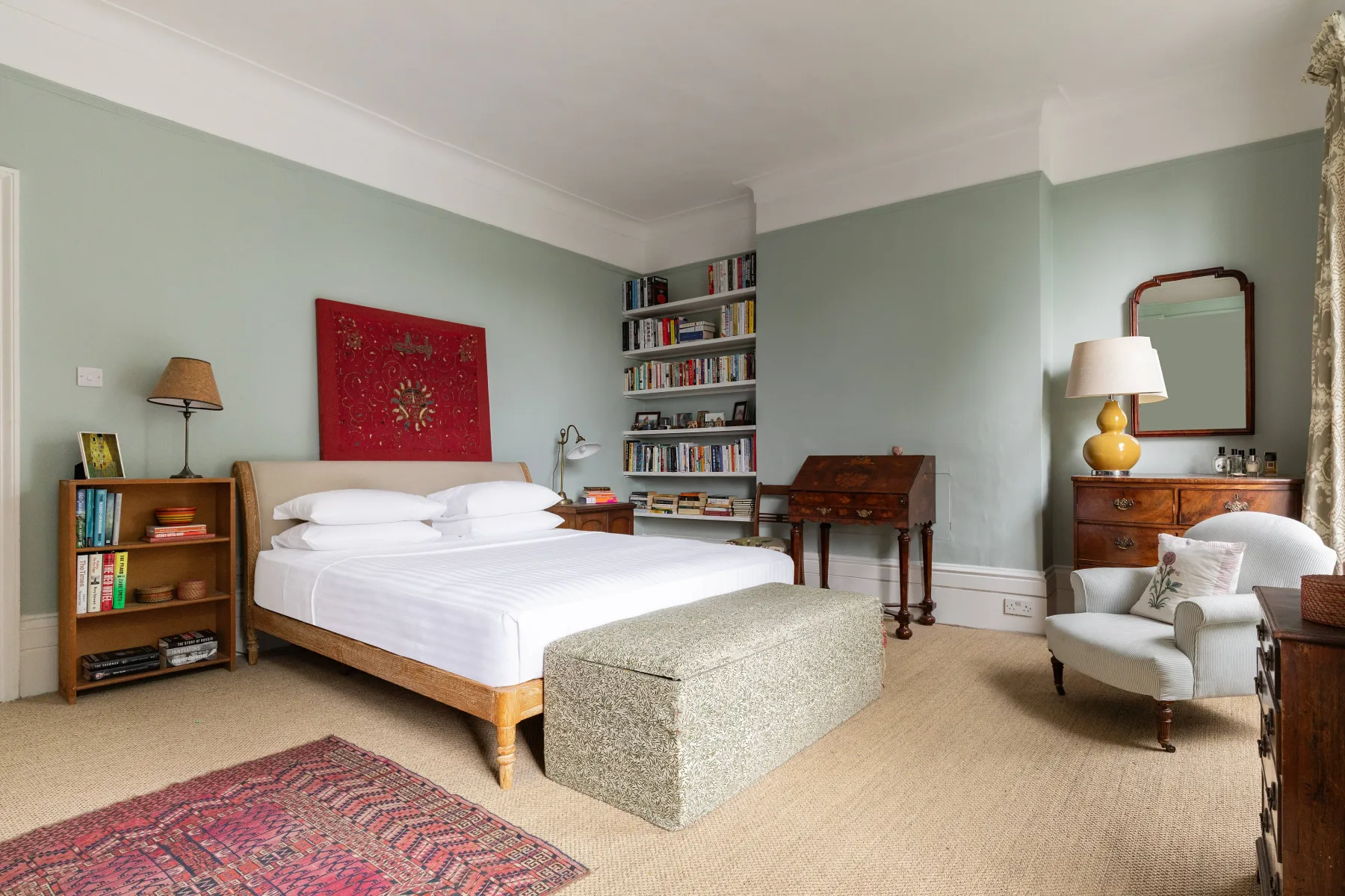 A bedroom with a neatly made bed, bookshelves, and a writing desk.