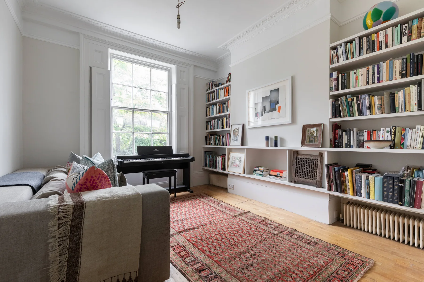 A bright living room with a piano, bookshelves, and a patterned rug.