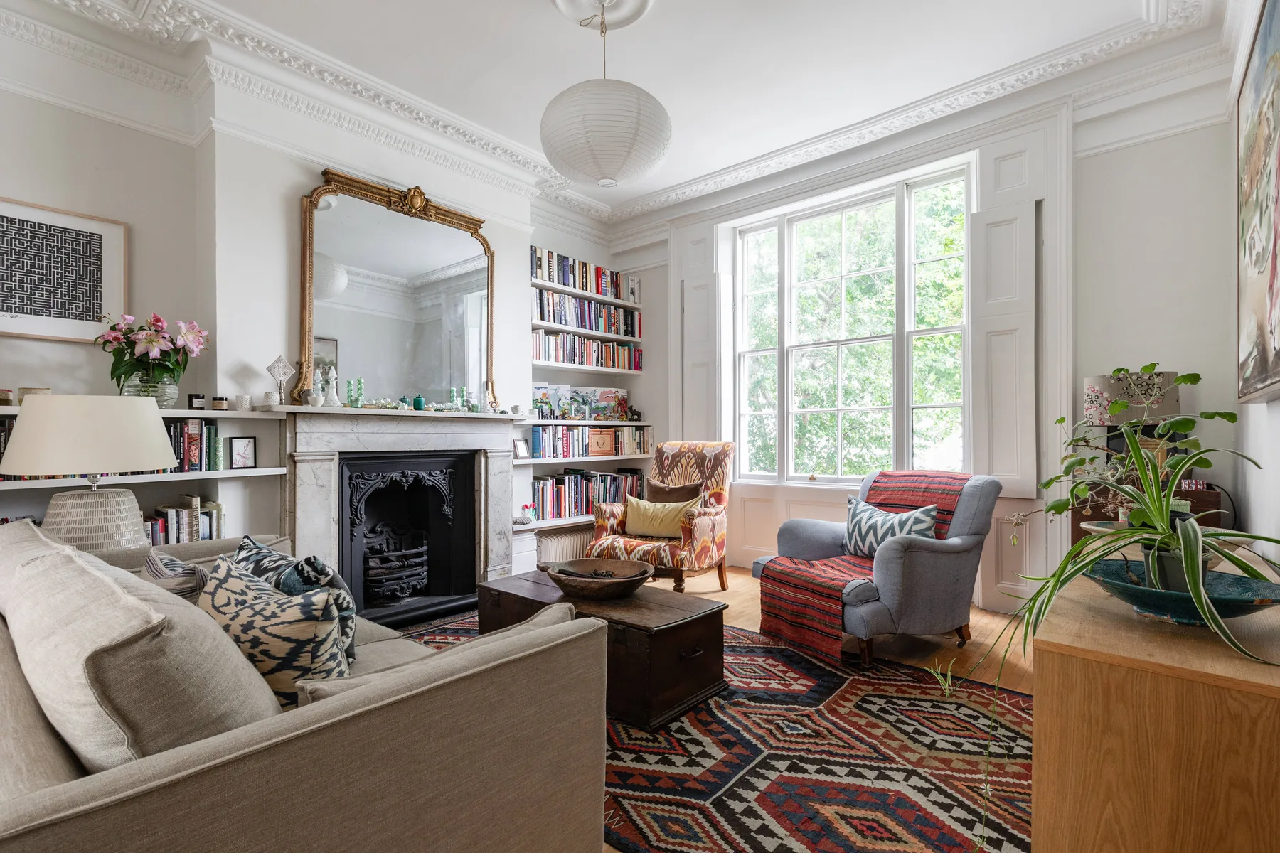 A bright living room with a fireplace, bookshelves, and seating around a patterned rug.