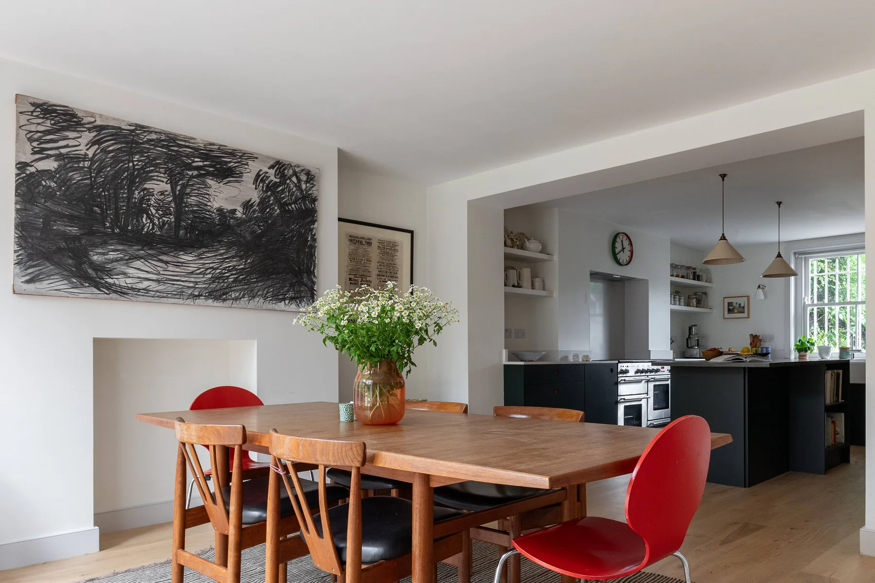 A dining area opens into a kitchen, with a wooden table and chairs beneath wall art.