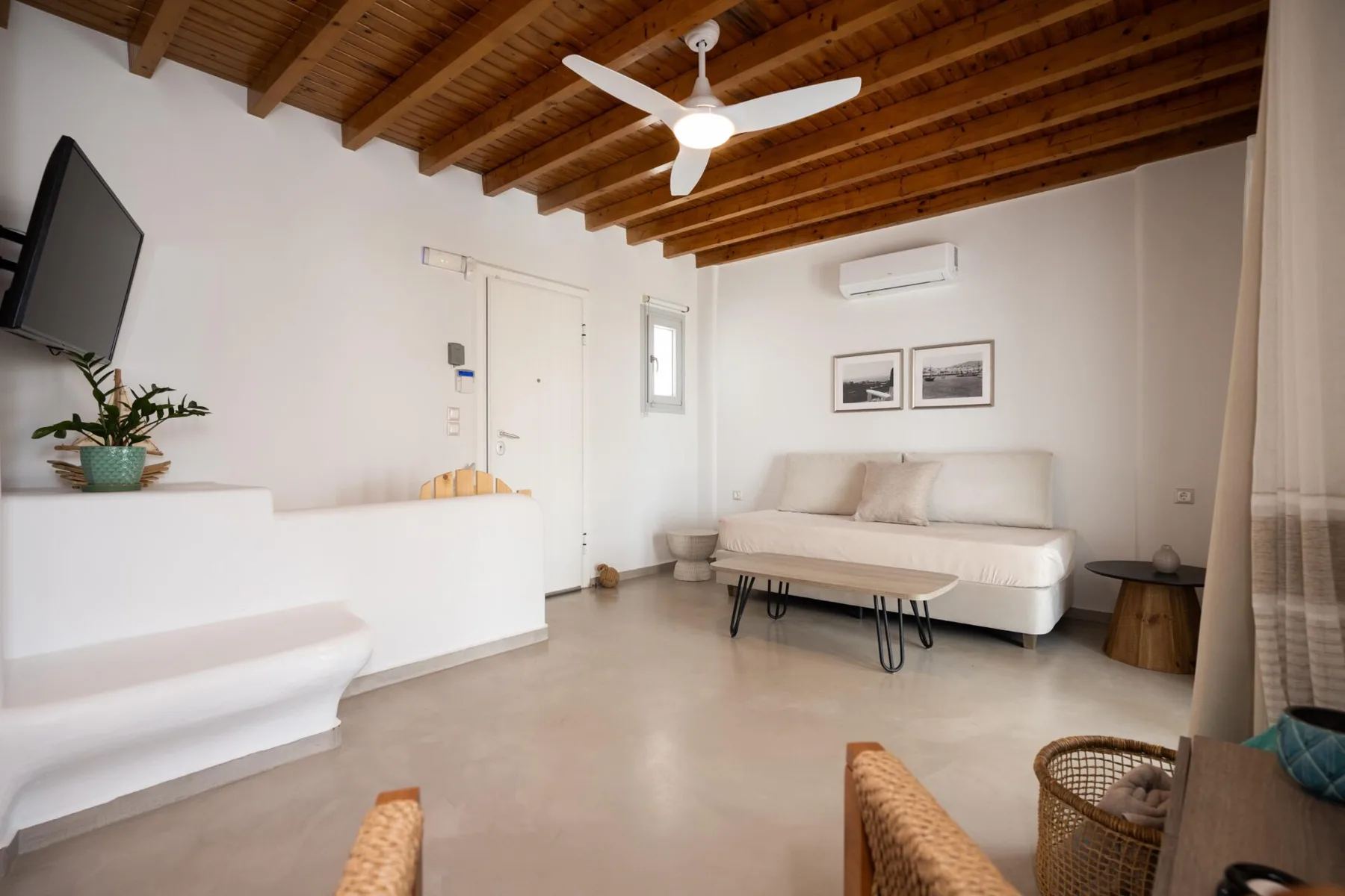 A bright living room with a white sofa and wooden ceiling beams.