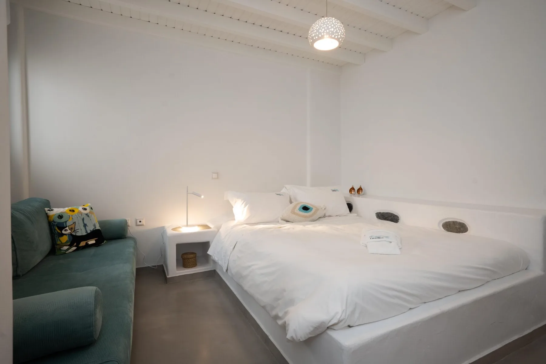 A bedroom with a white bed and a teal sofa beside it.