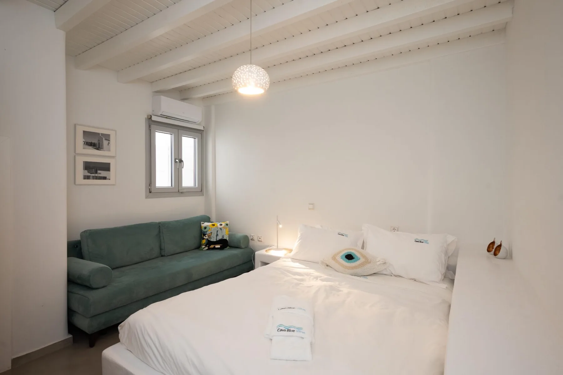 A bedroom with a white bed and a green sofa beside the window.
