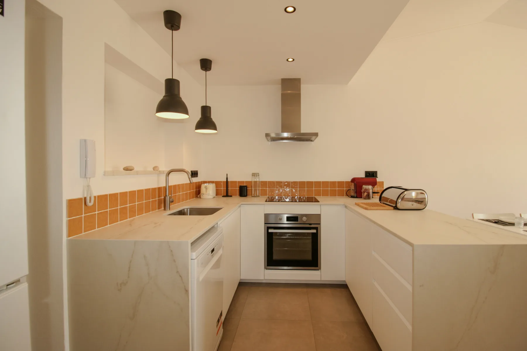 Una cocina moderna con encimeras claras y salpicadero de azulejos naranjas.