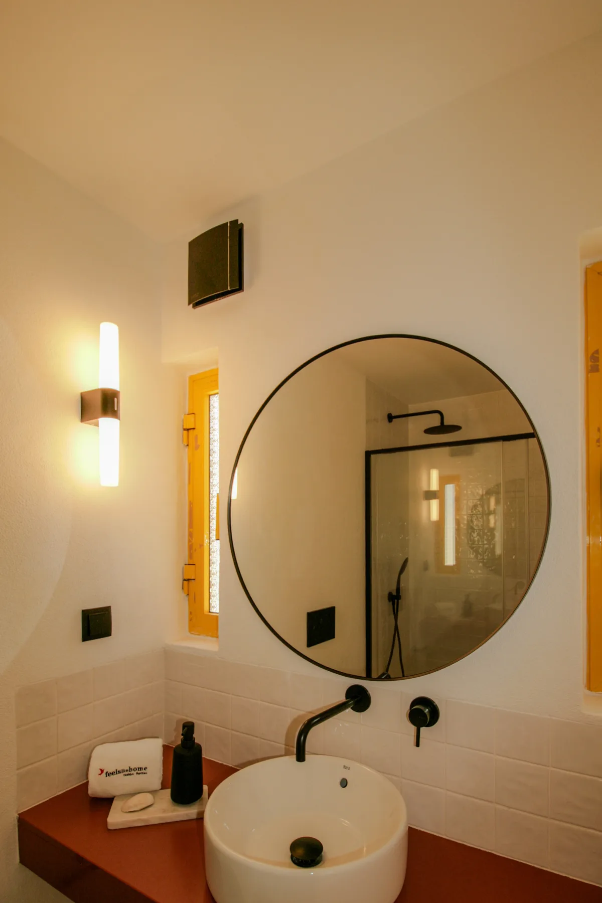 Baño con un espejo redondo sobre un lavabo de sobreponer.
