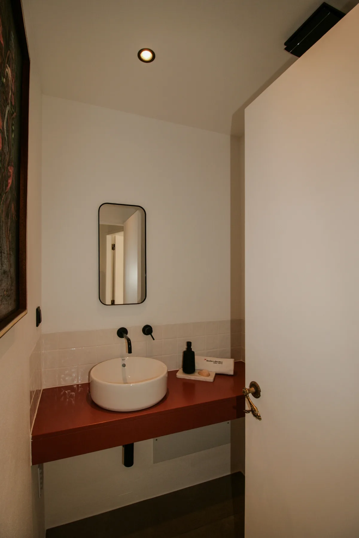 Baño con un lavabo redondo sobre una encimera roja y un espejo de pared.