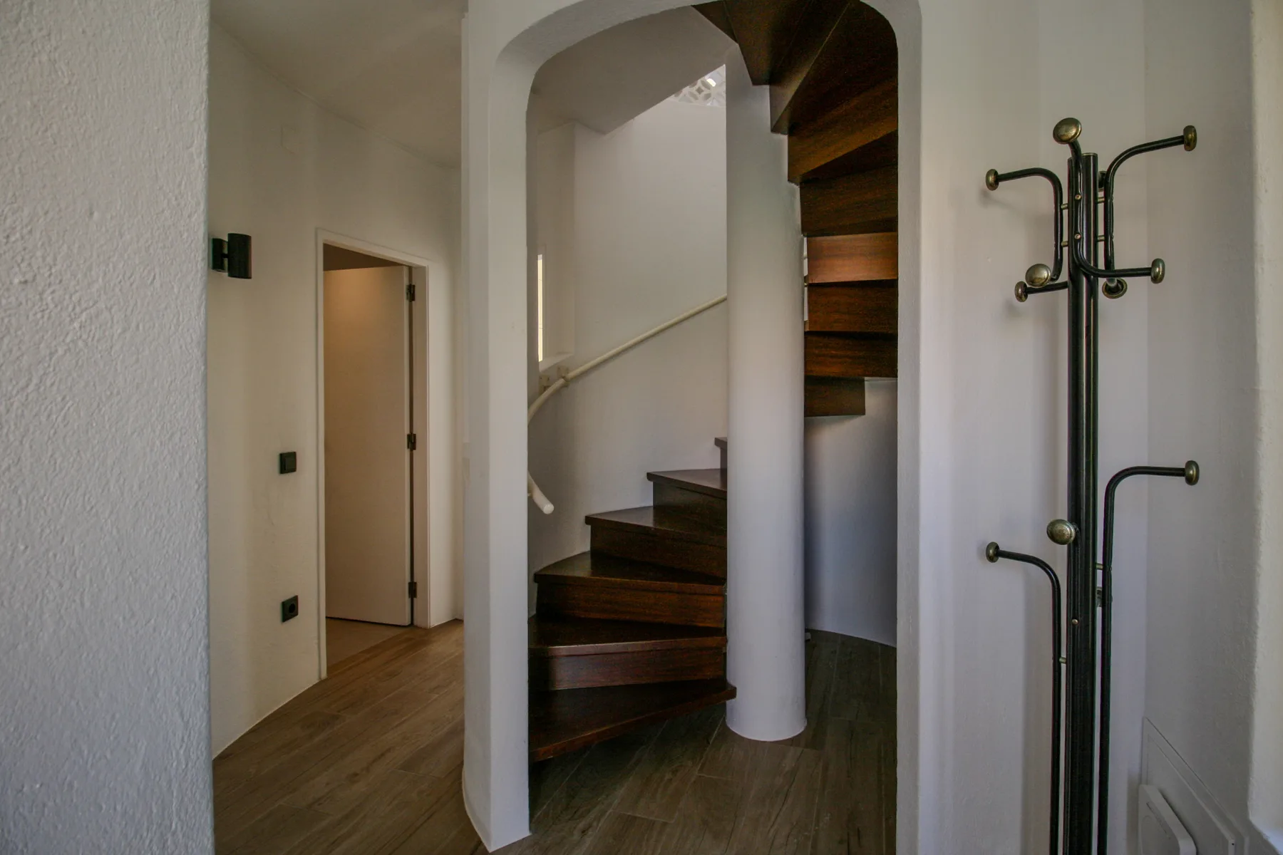 Un hueco de escalera interior con una escalera curva de madera y un perchero.