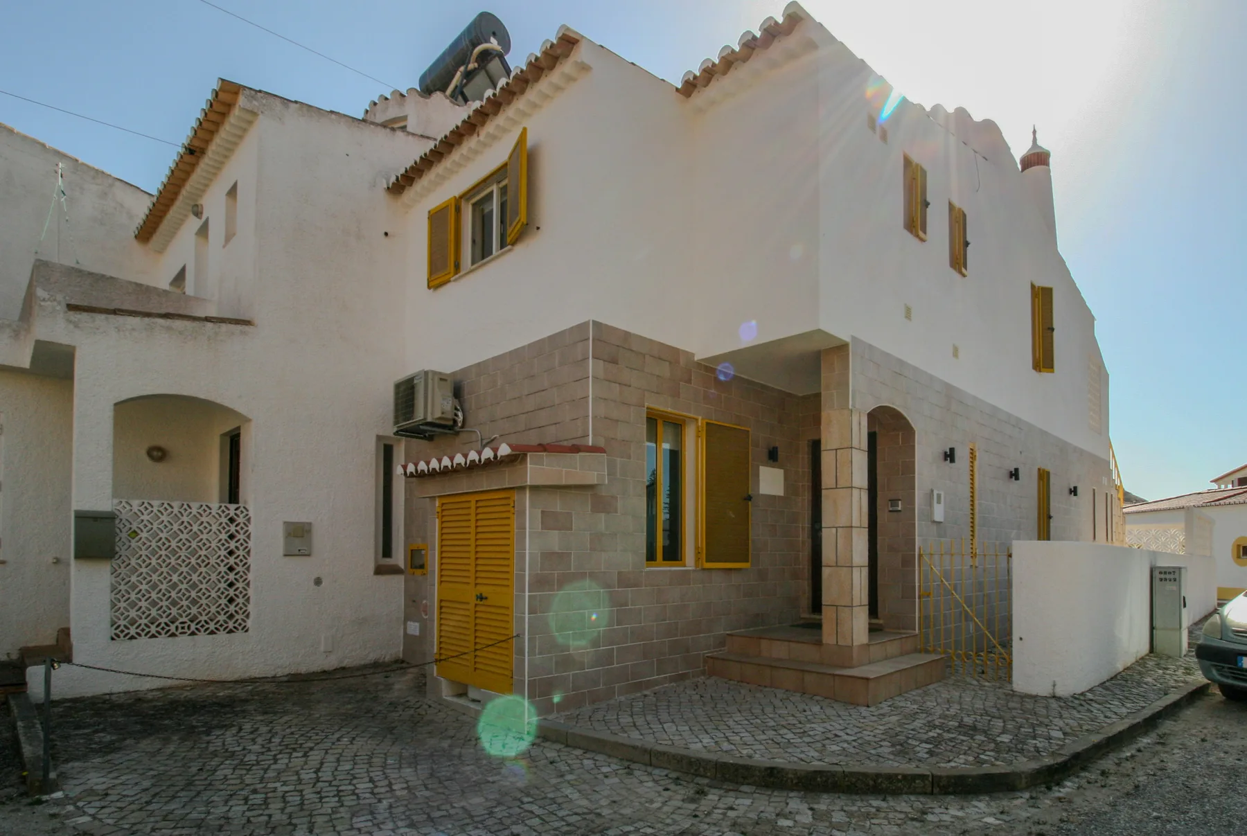 Una casa blanca de varias plantas con contraventanas amarillas da a una calle empedrada.