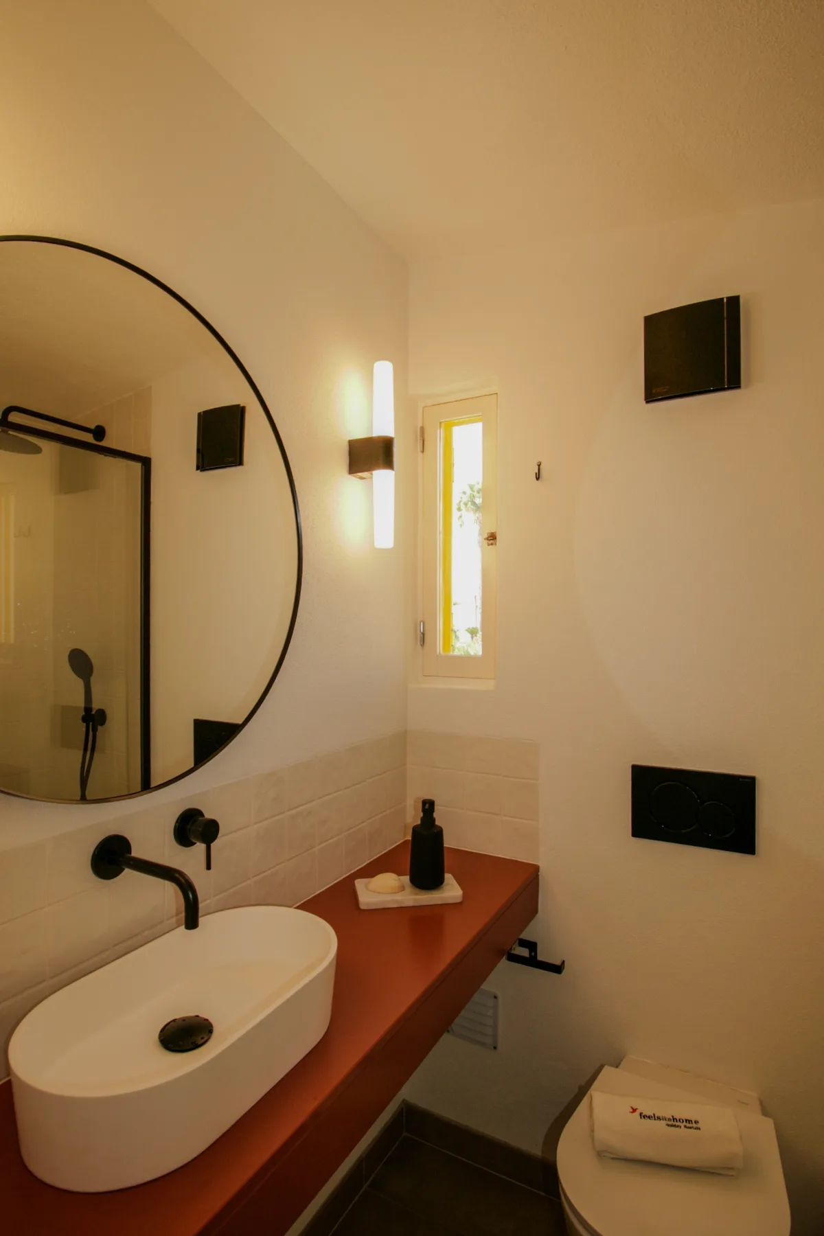 Un baño con lavabo sobre la encimera y un espejo redondo en la pared.