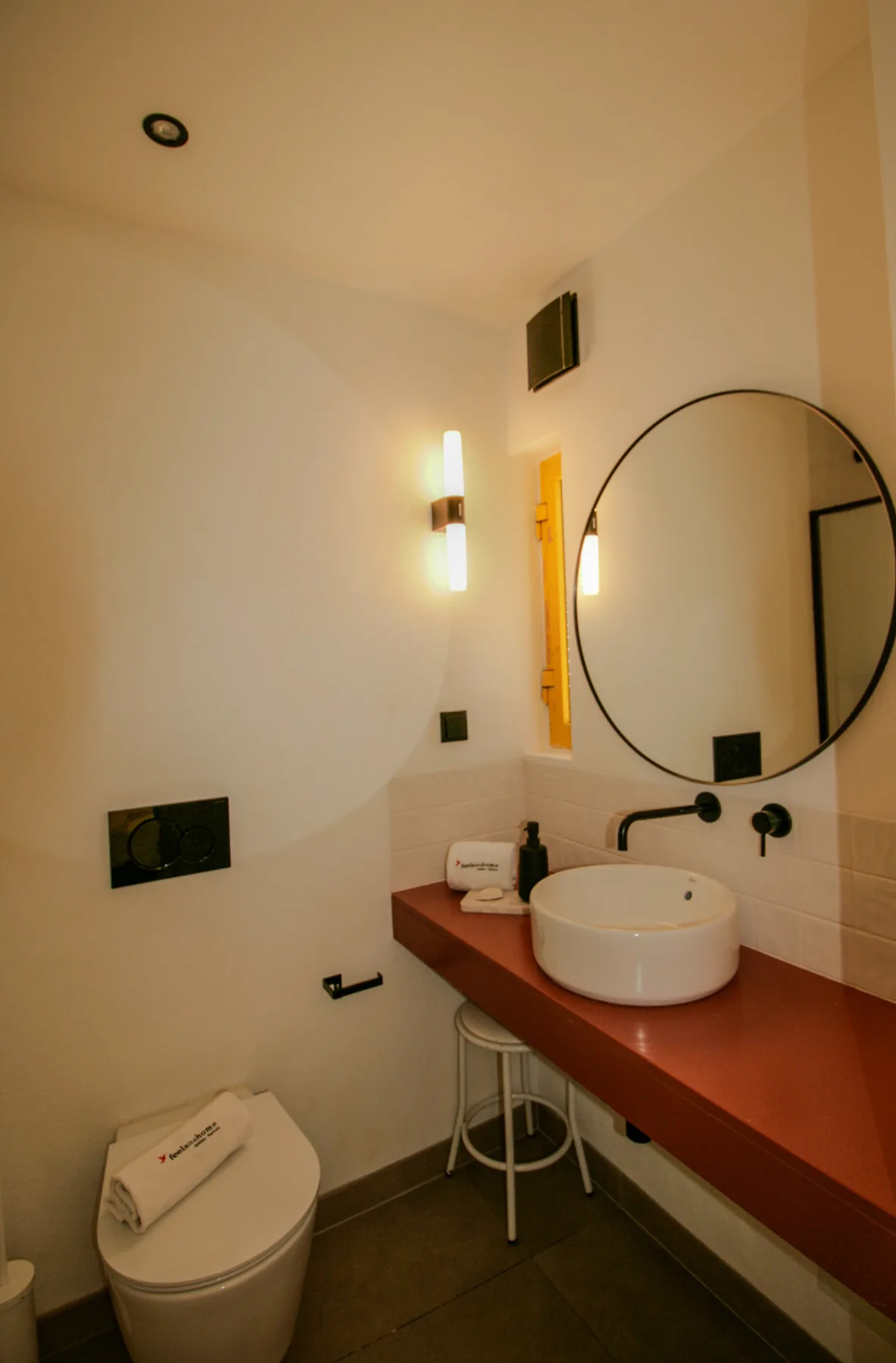 Un baño con lavabo, espejo redondo e inodoro.