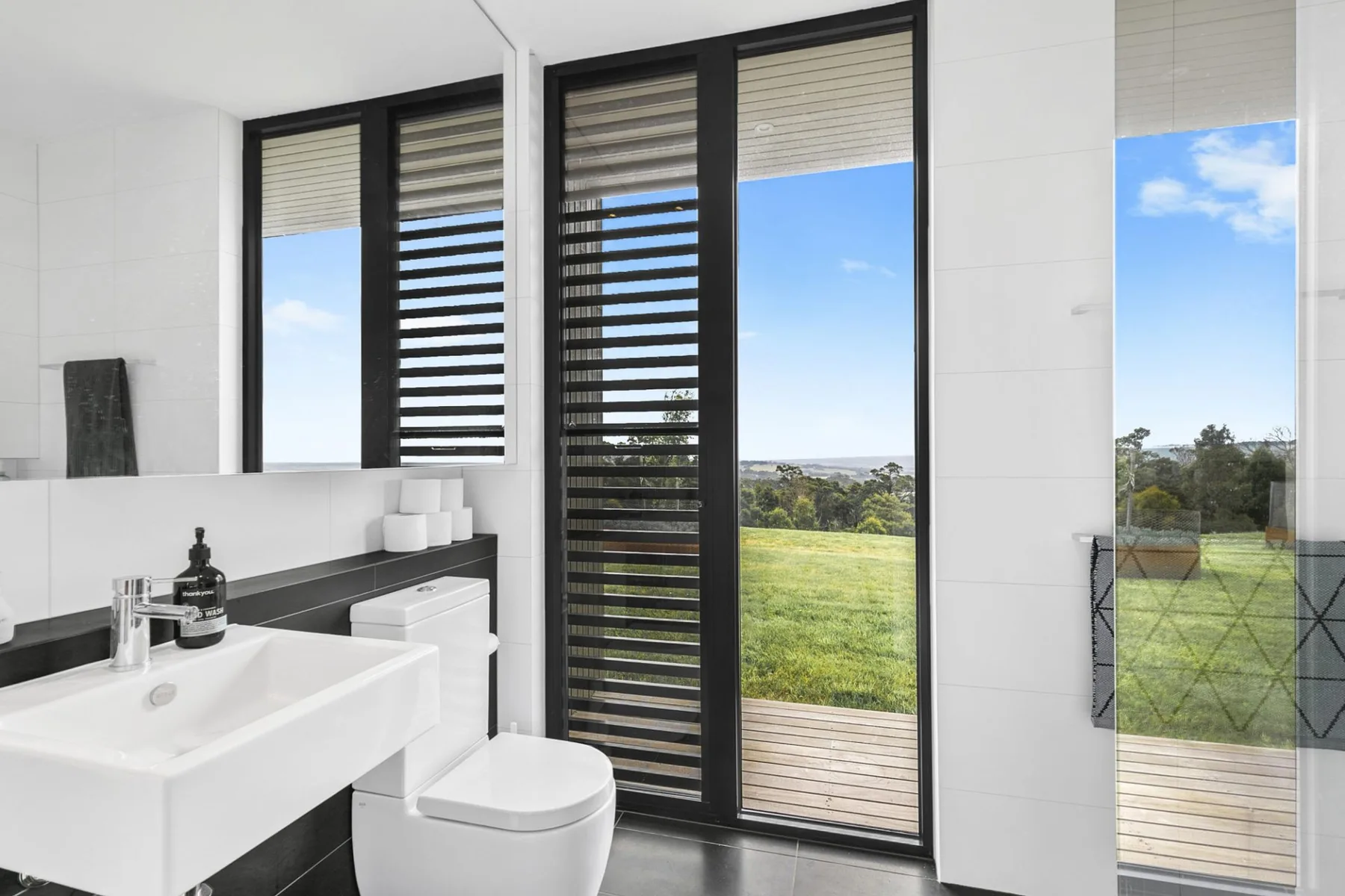 A bright bathroom with a sink, toilet, and large windows overlooking a green landscape.