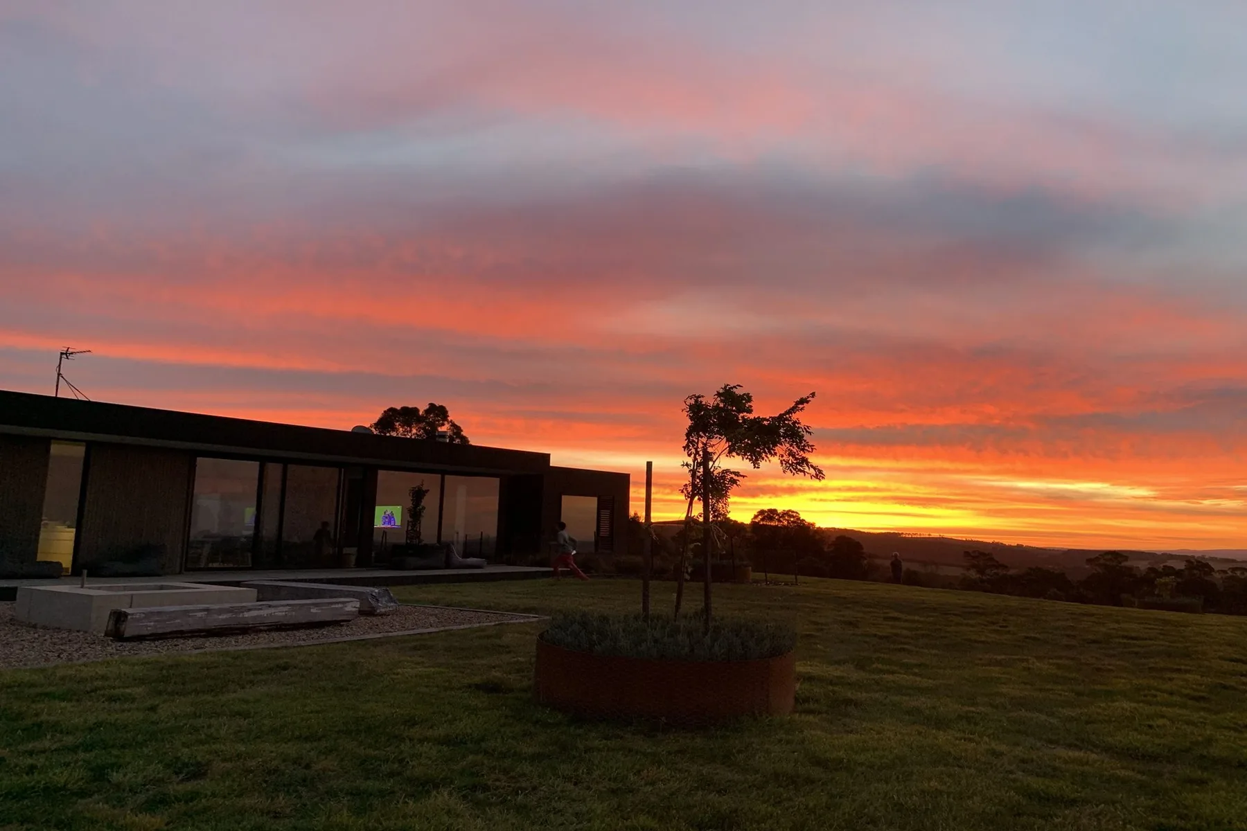 A modern building and landscaped grounds sit beneath a vivid sunset sky.