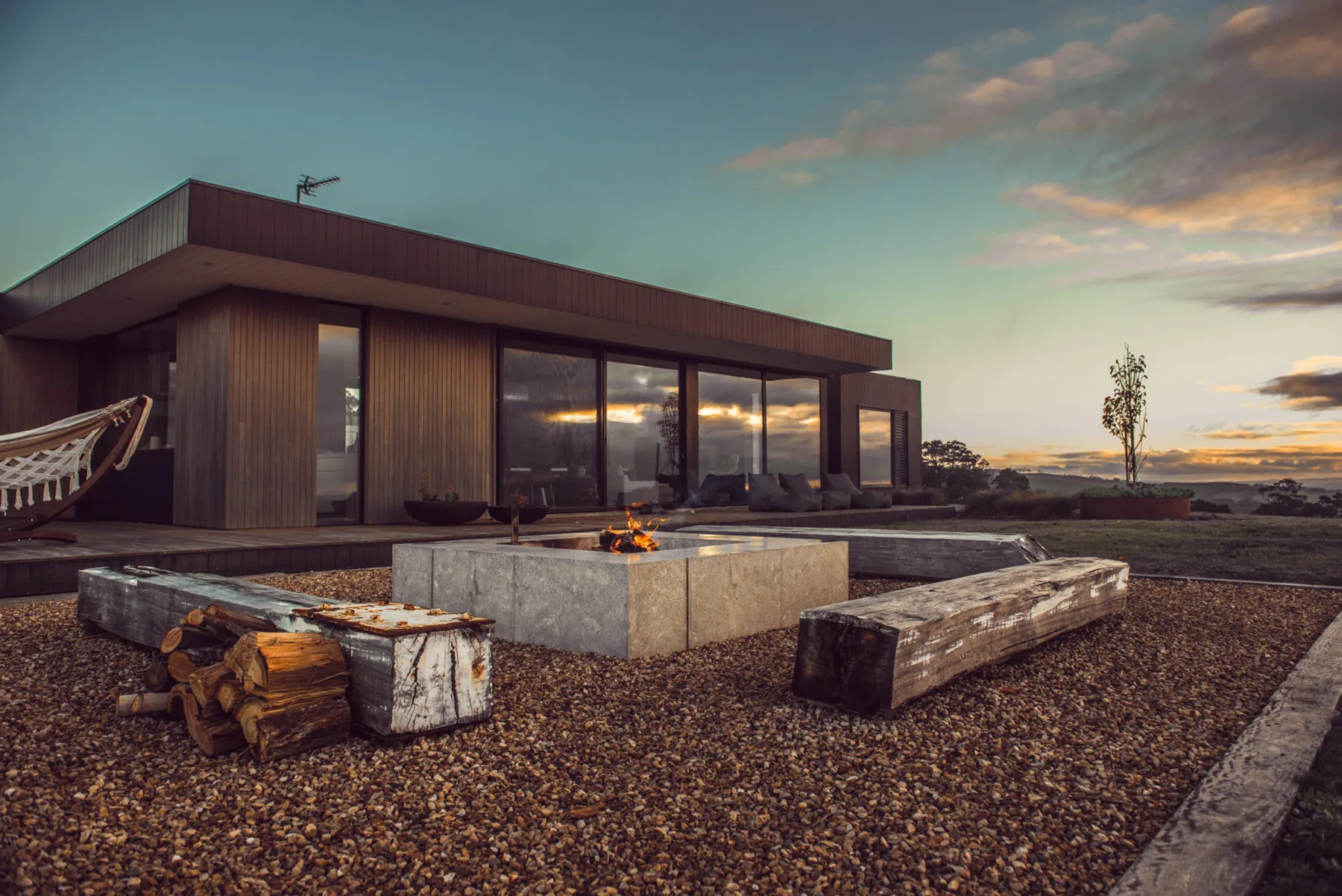 A modern house with large windows and an outdoor fire pit at sunset.