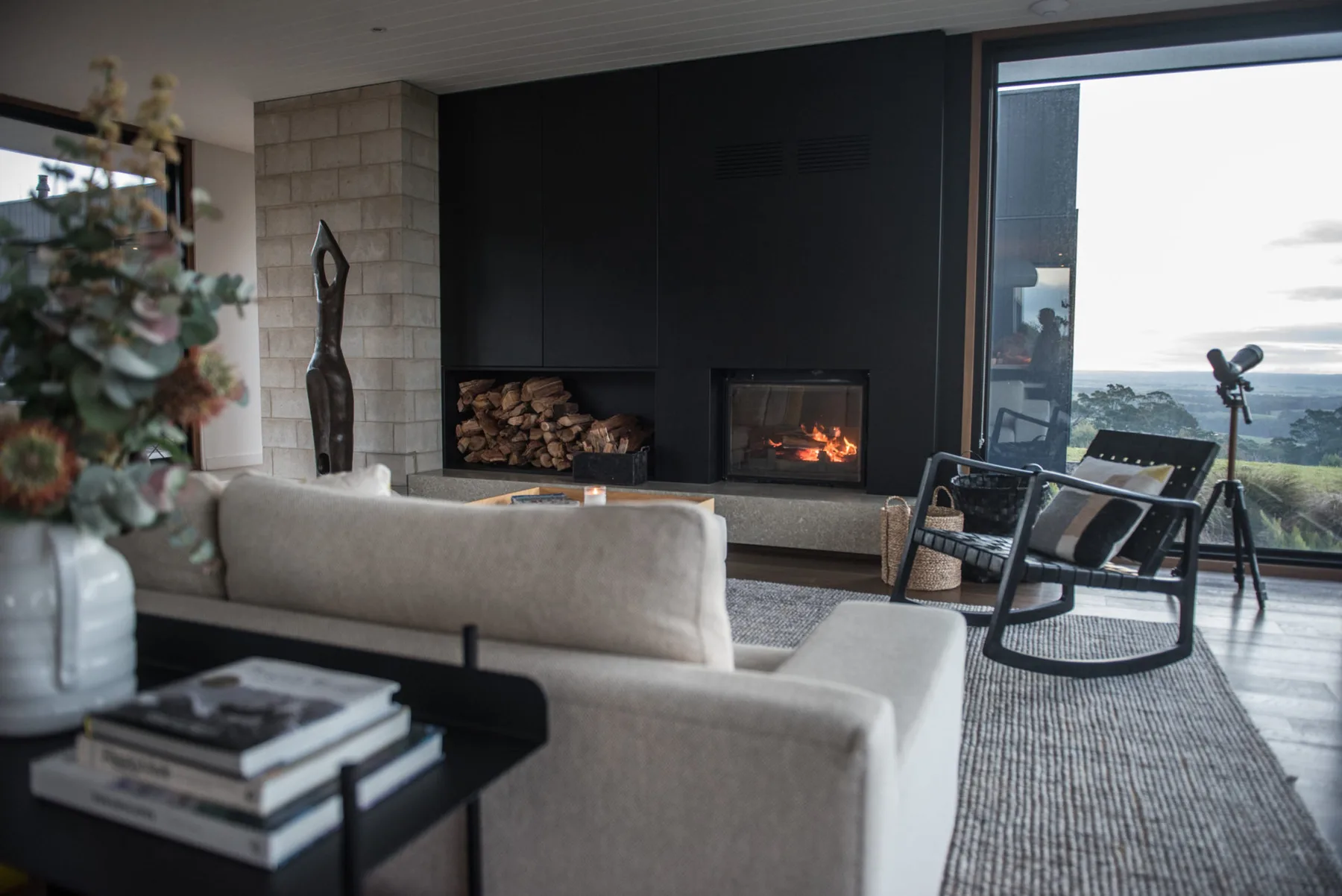 A modern living room with a fireplace and seating beside large windows.