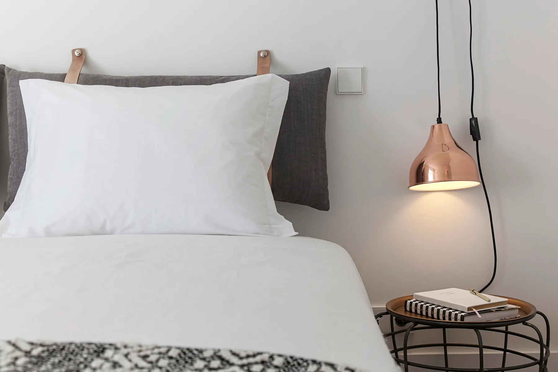 A neatly made bed with white bedding sits beside a lit pendant lamp.
