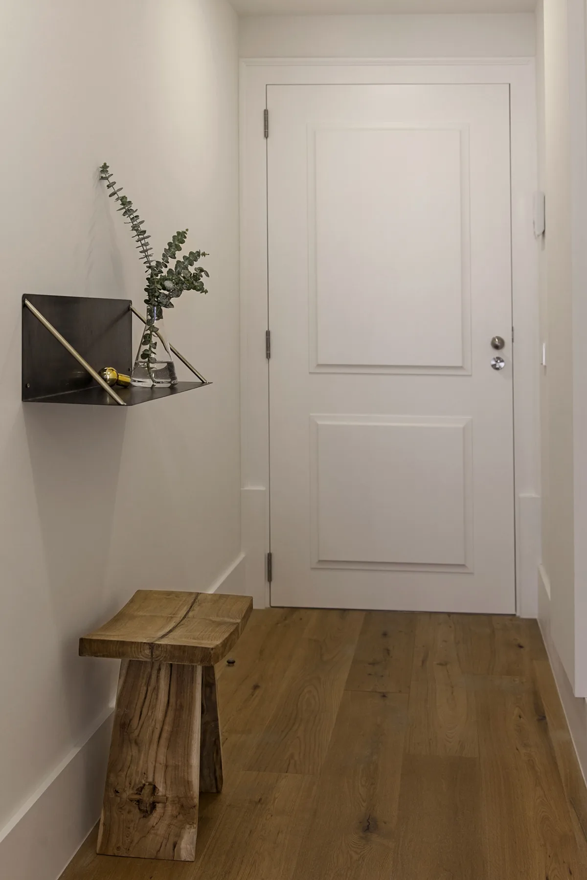 A narrow entryway with a wooden bench beside a white door.