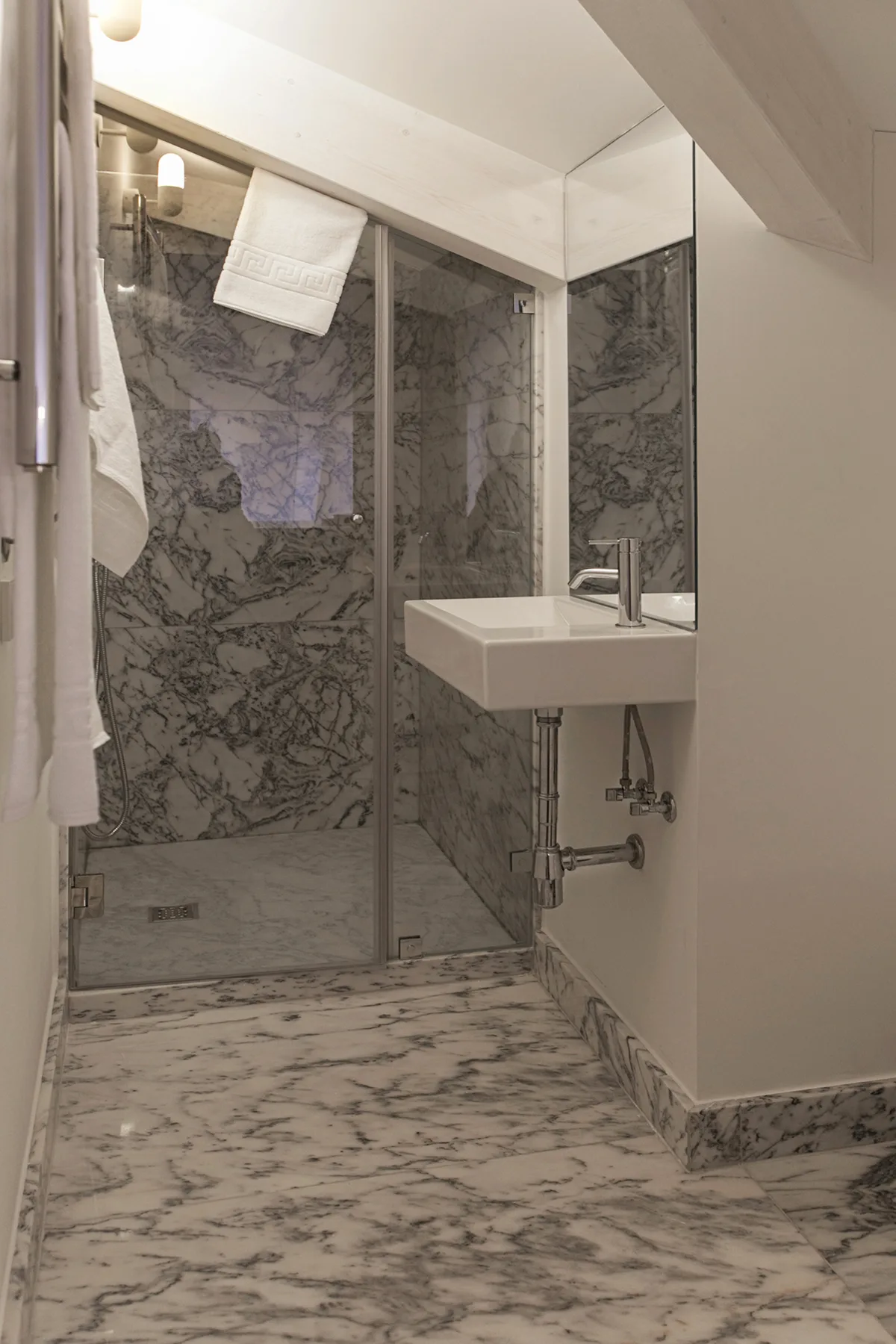 A bathroom with a glass shower, a wall-mounted sink, and patterned surfaces.