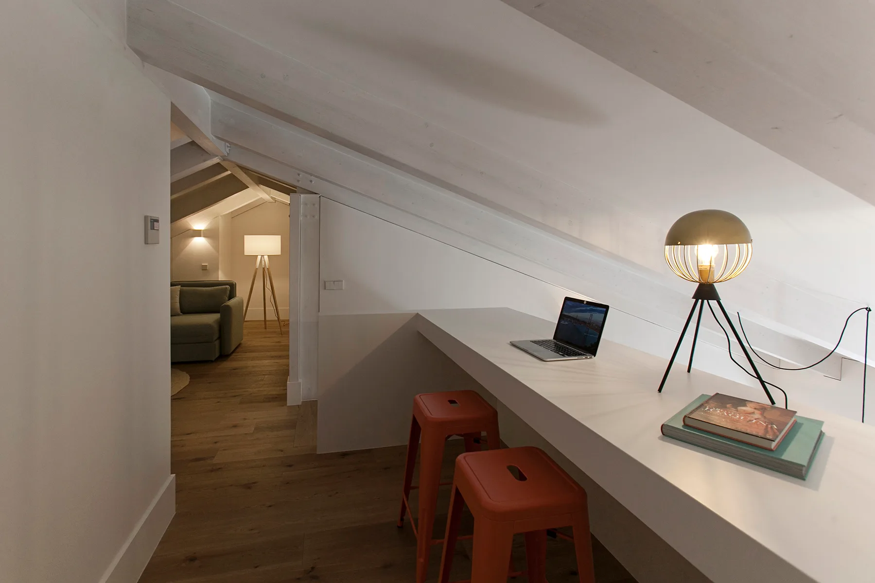 A sloped-ceiling loft workspace with a desk, stools, and an open laptop.