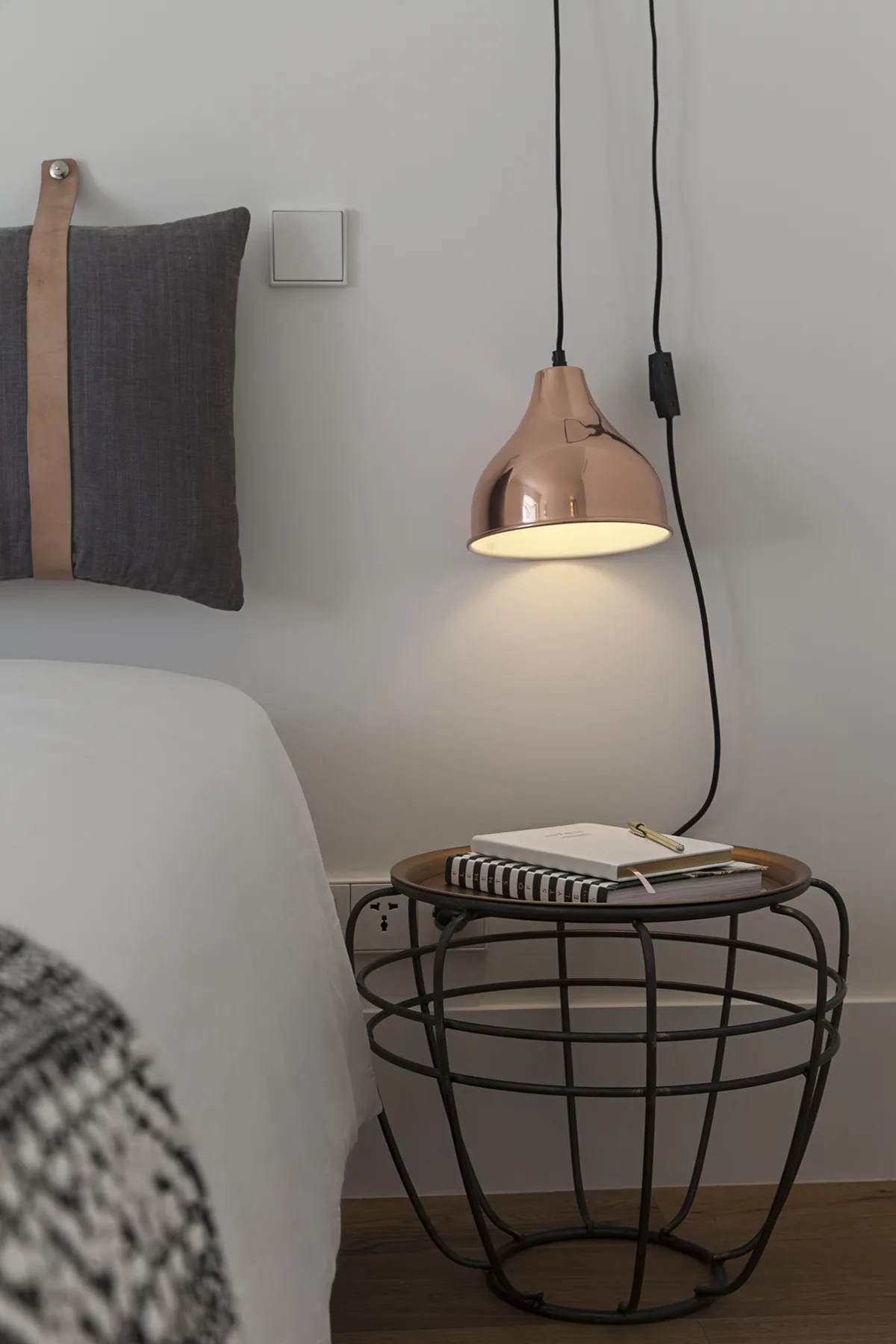 A bedroom corner with a bedside table, a hanging lamp, and a neatly made bed.