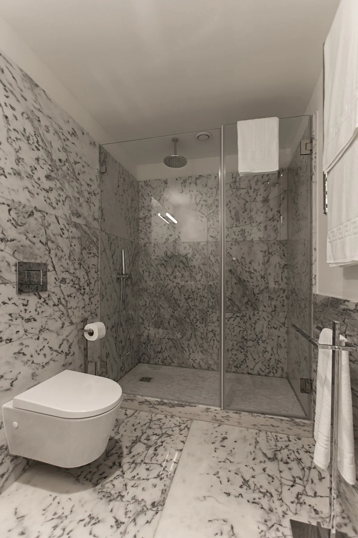 A bathroom with a wall-mounted toilet and a glass-enclosed shower.