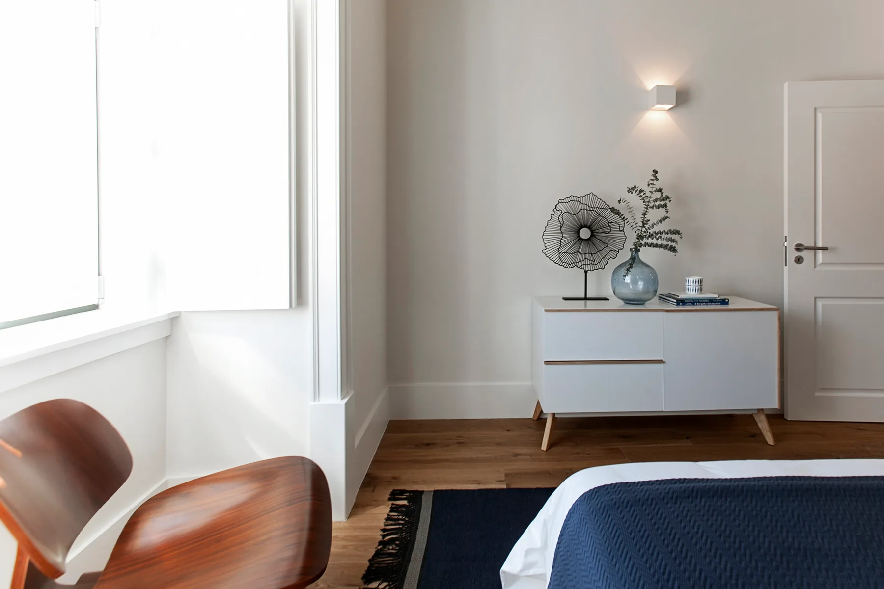 A bright bedroom with a bed, wooden seating, and a low cabinet.