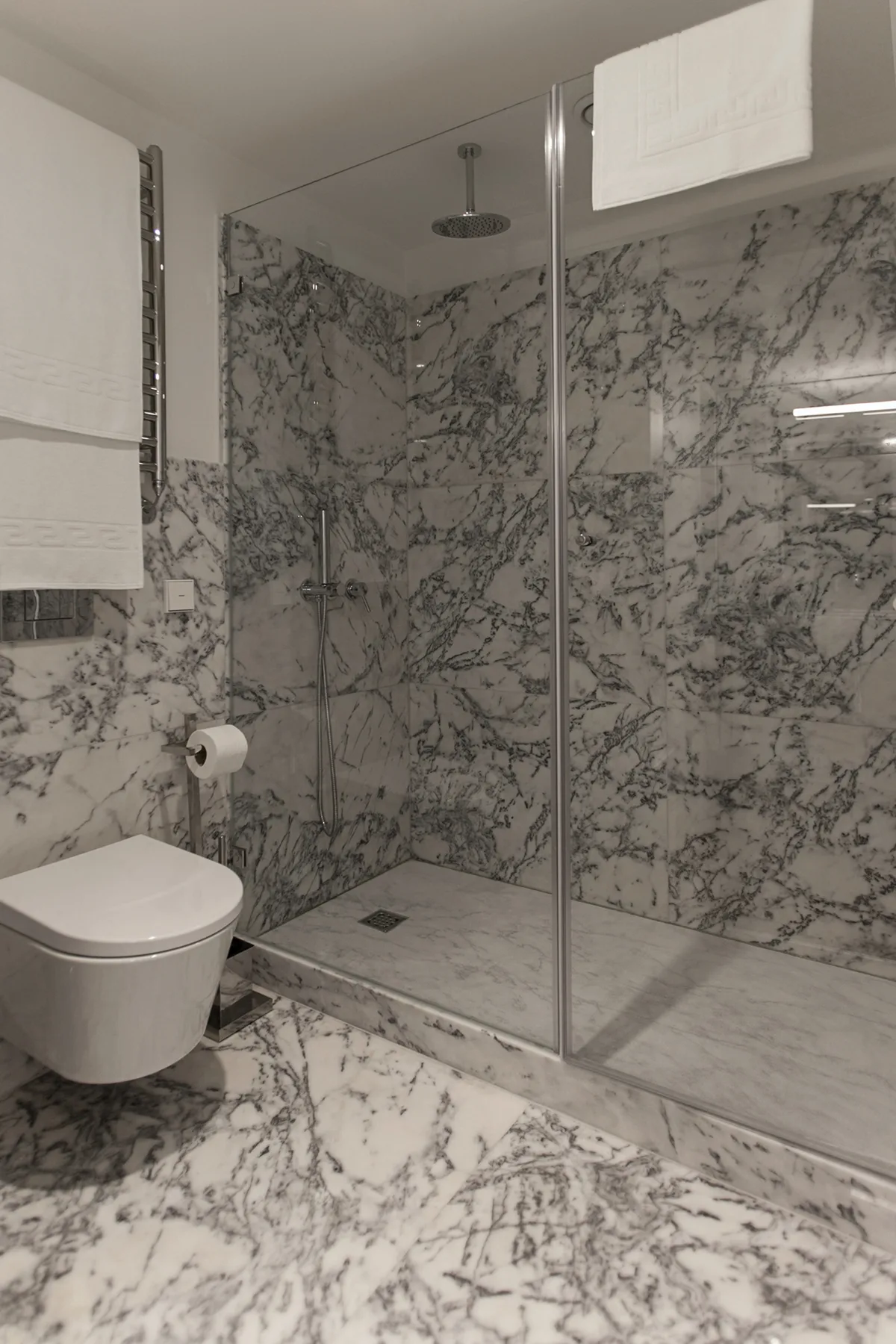 A bathroom with a glass shower and wall-mounted toilet.