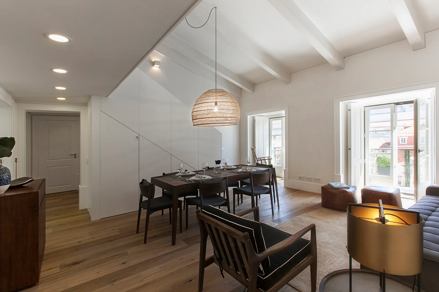A bright dining area with a long table and chairs beside large windows.