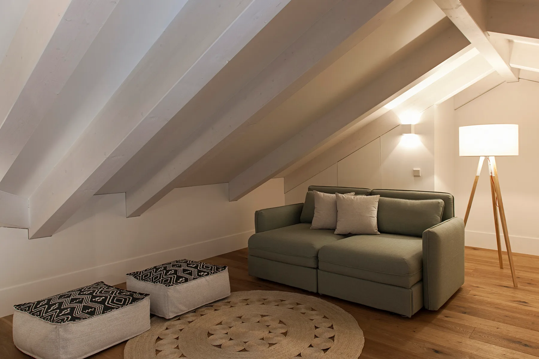 A cozy living area with a green sofa, patterned floor cushions, and a standing lamp.
