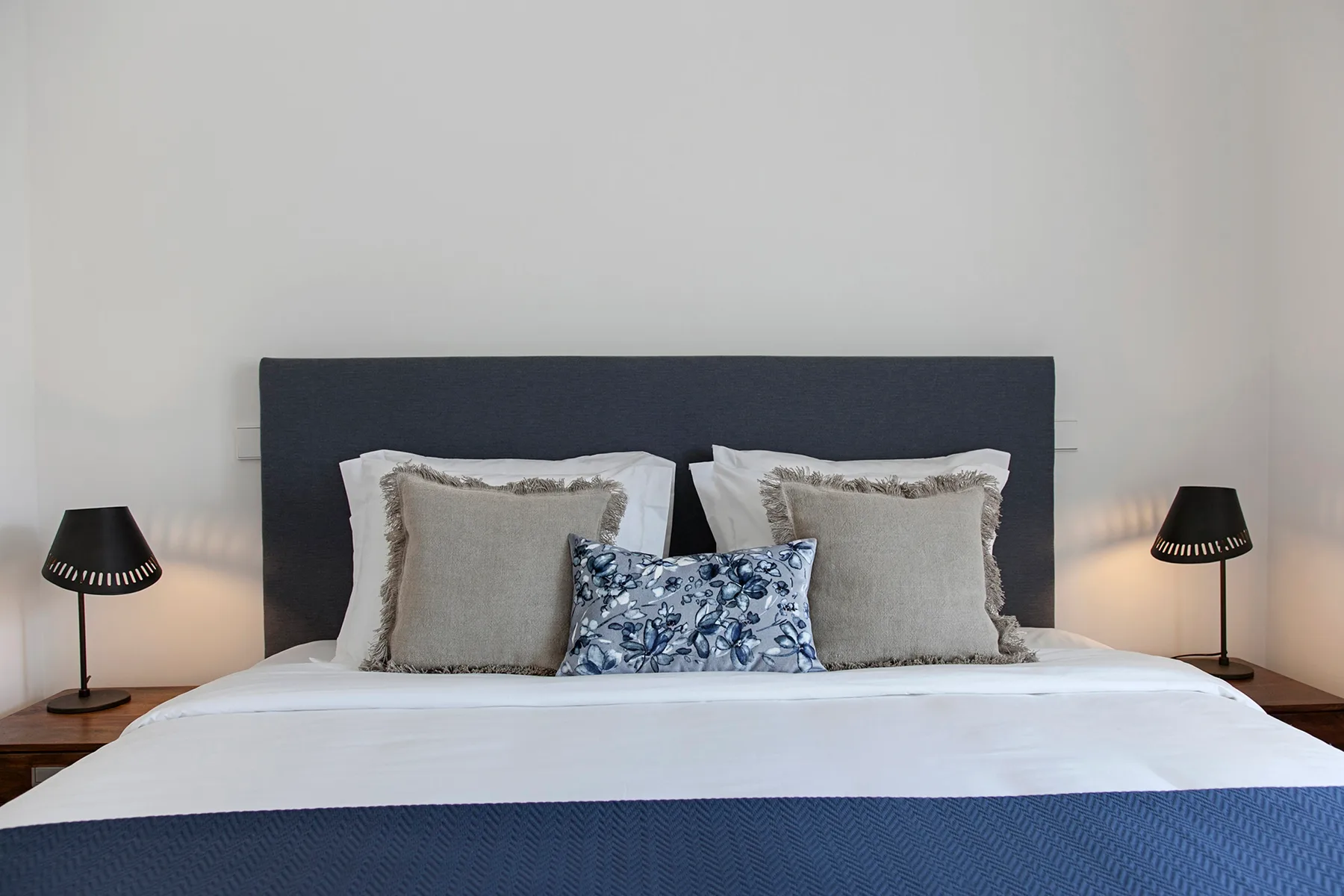 A bedroom with a neatly made bed, patterned cushion, and matching bedside lamps.
